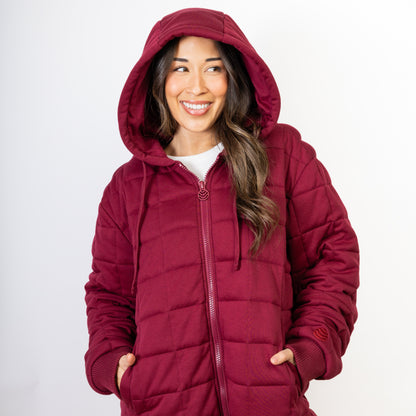 A woman wearing a burgundy red weighted Therahoodie with the hood up, standing against a white background.